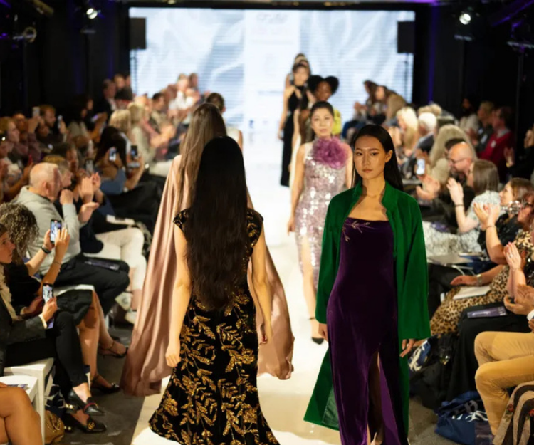 Models walk the catwalk at Central London Alliance's London Fashion Week event, wearing rich green and gold velvet outfits, with photographers and audience in the background
