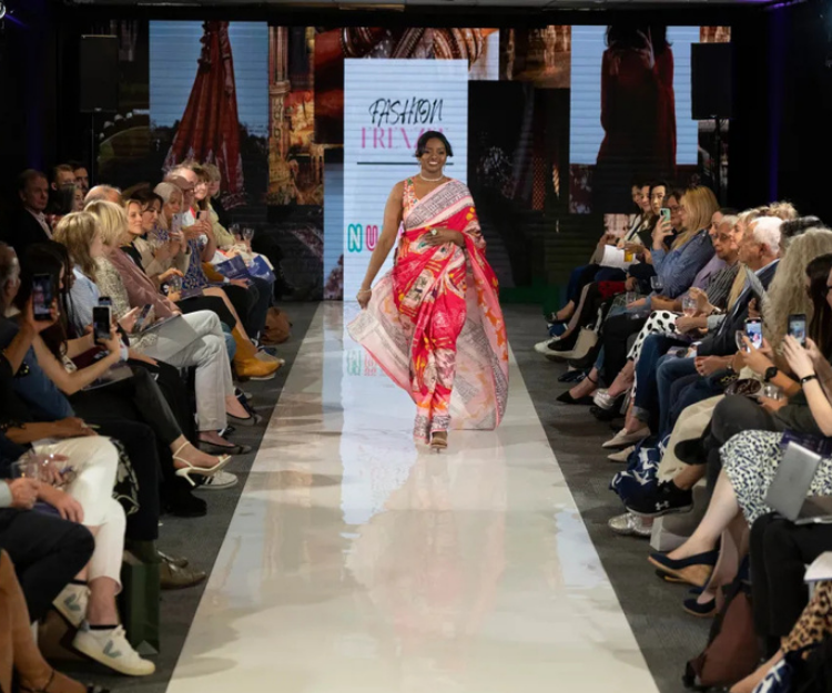 Model walks the runway at Central London Alliance's London Fashion Week show wearing a red sustainable sari, with audience seated on both sides