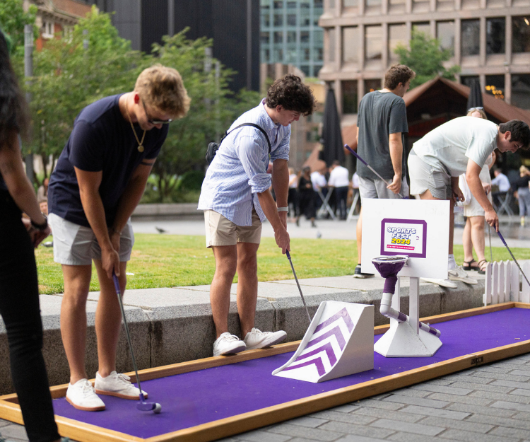 Group of people playing mini golf on a purple course installed outdoors in the City of London, part of the Summer of Sport in the City campaign