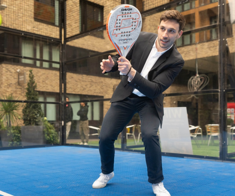 Man in business attire playing padel on an outdoor court, part of a corporate sports challenge during Summer of Sport in the City