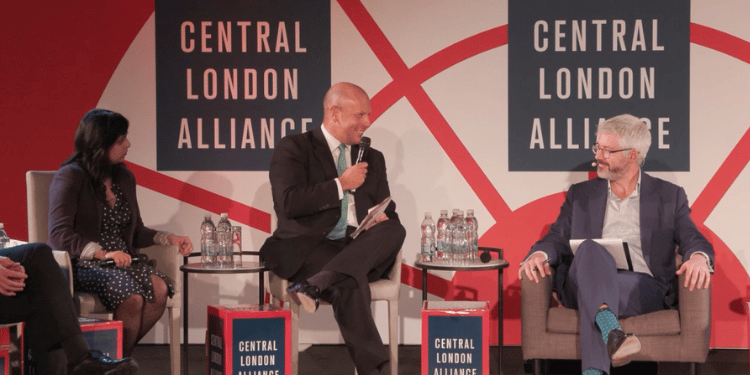 Three panelists seated in armchairs on stage, one speaking into a microphone with his hand raised, in front of 'Central London Alliance' branded backdrop panels