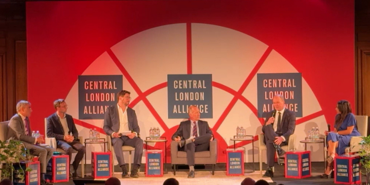 Five panelists seated in armchairs on stage in discussion, in front of a red and white 'Central London Alliance' backdrop with water bottles on side tables